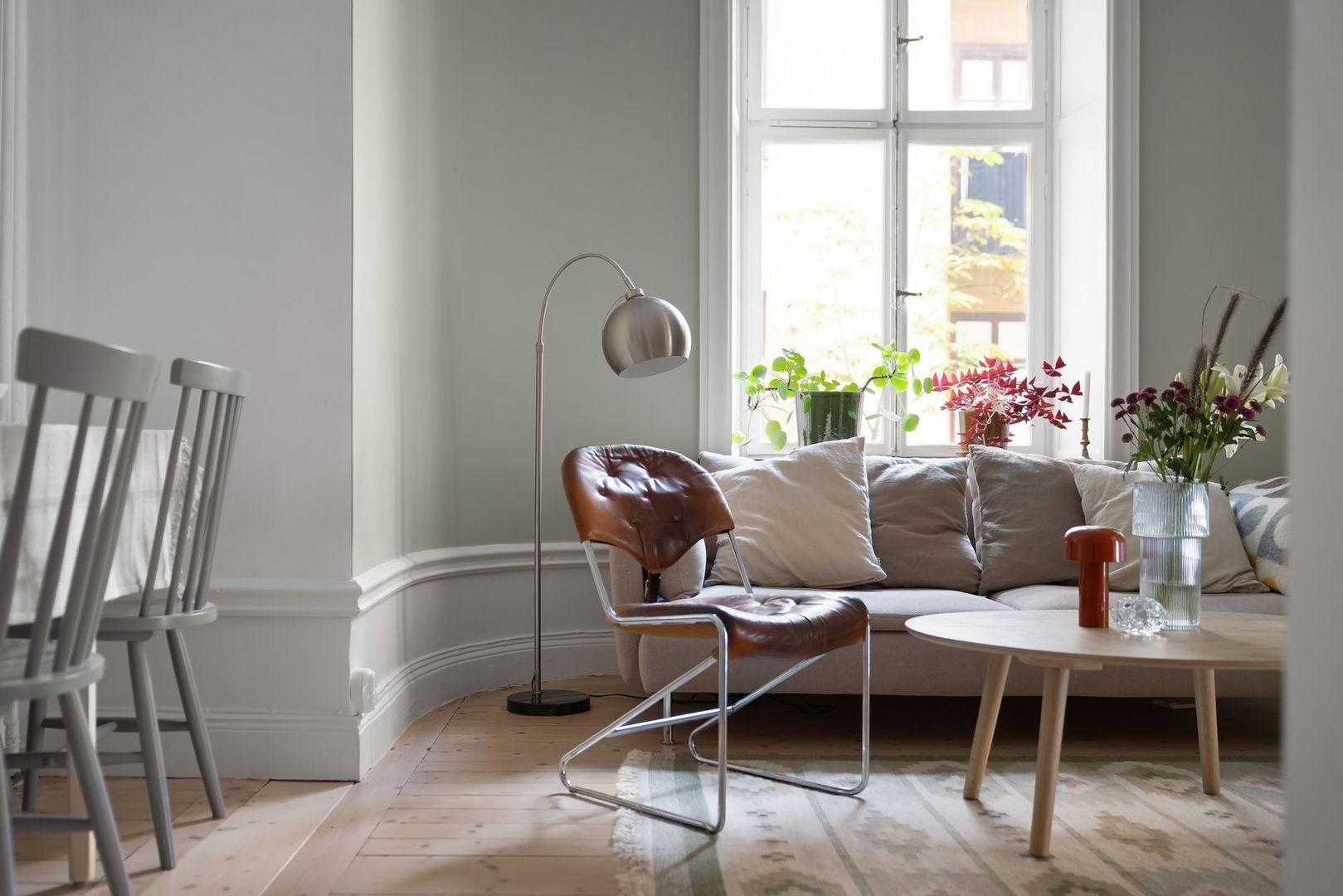 Ljust nordiskt vardagsrum med golvlampa, fåtölj och blomvaser