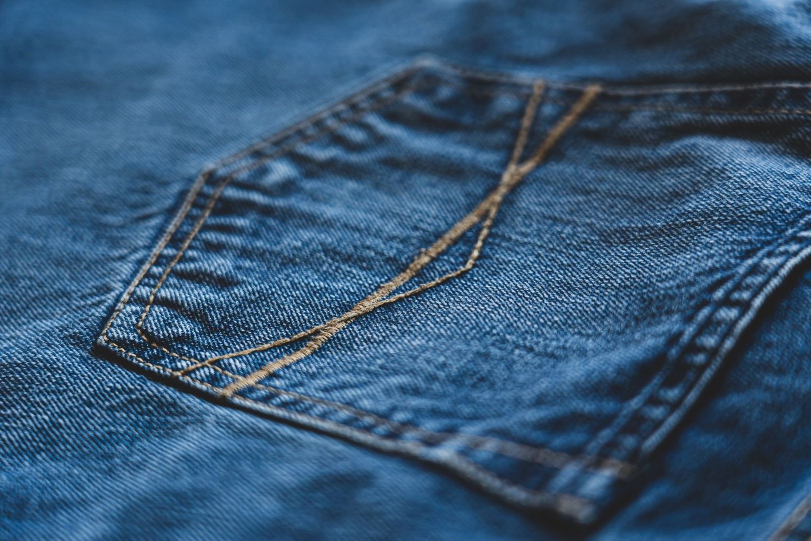 Närbild av blå denim med synliga, korsande lagningar i beige tråd